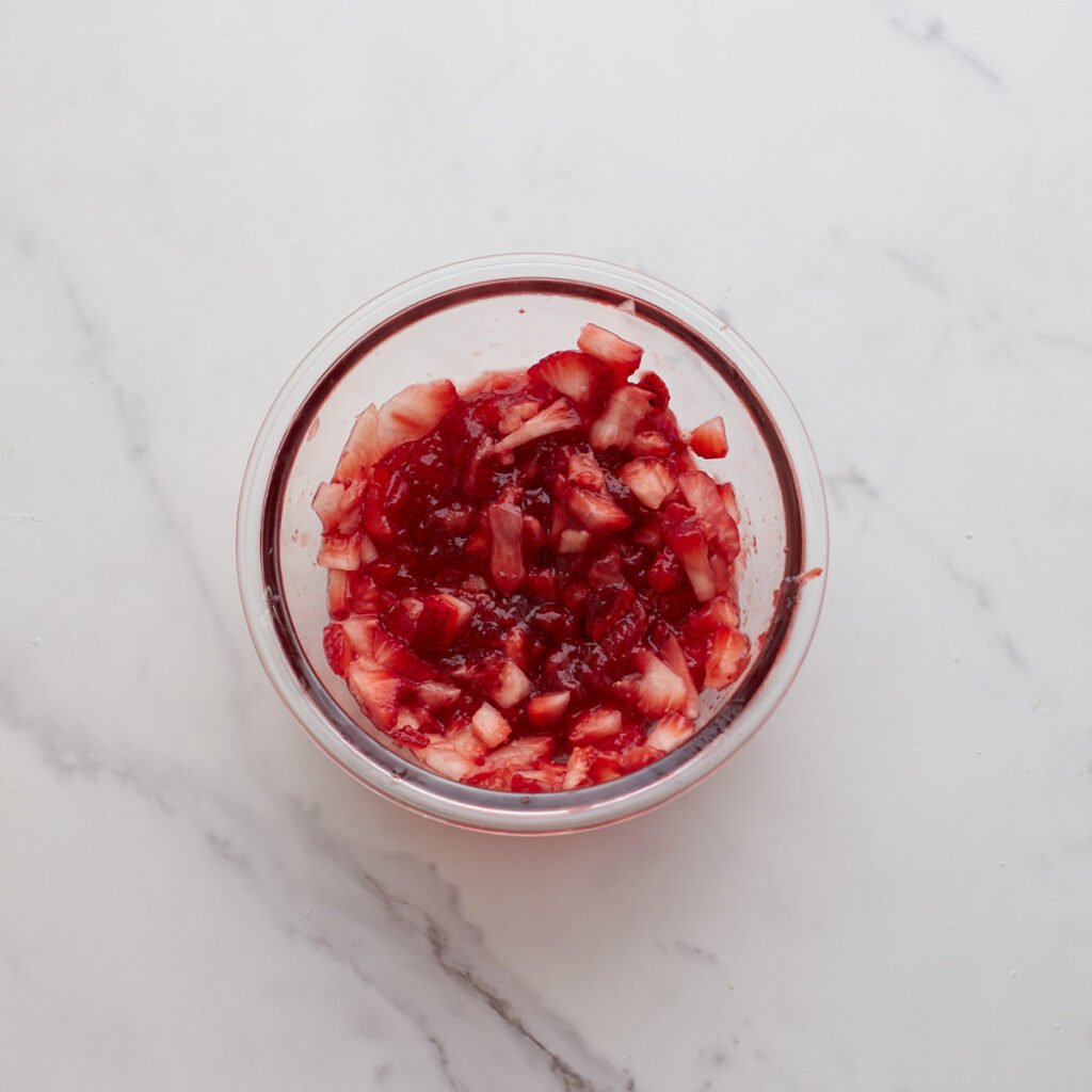 diced up strawberries in a glass bowl mixed with strawberry jam