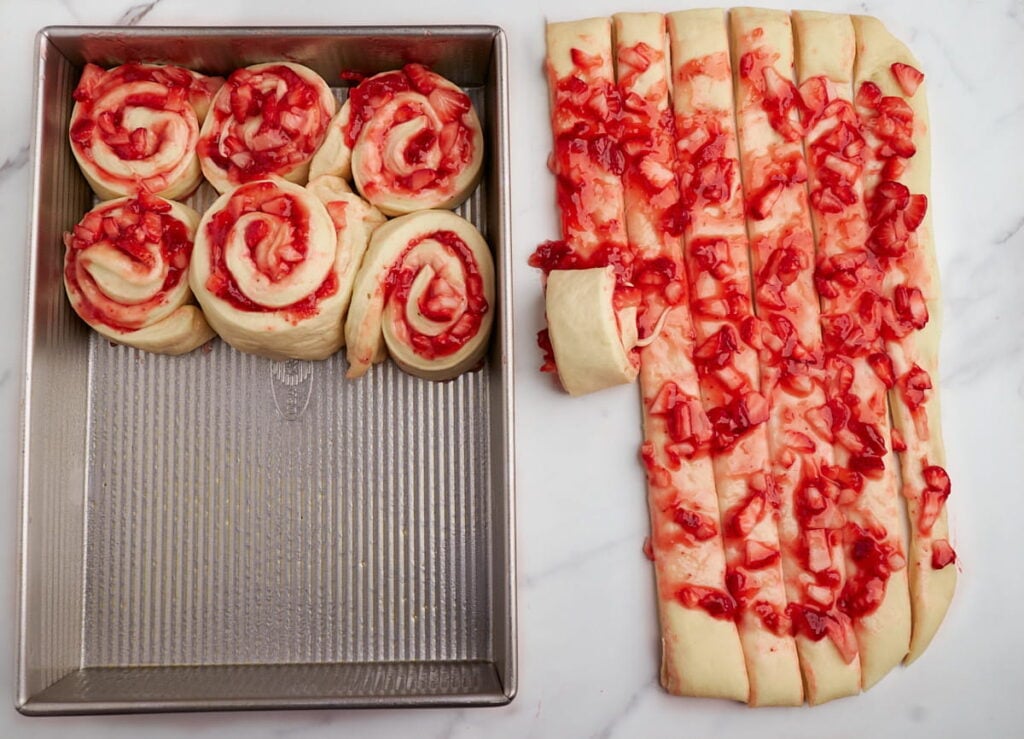 9x13 pan of sourdough strawberry rolls with some still being rolled up