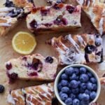 slices of lemon blueberry sourdough focaccia with lemon glaze on top next to a bowl of blueberries