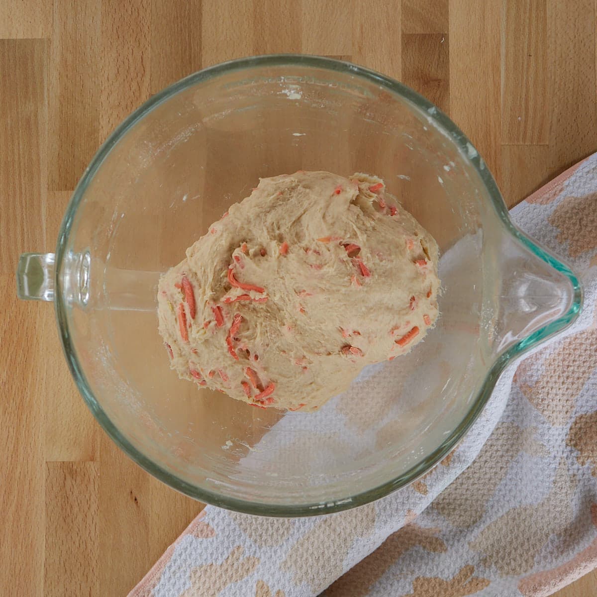 Carrot cake cinnamon roll dough in a glass bowl on a wood board. 