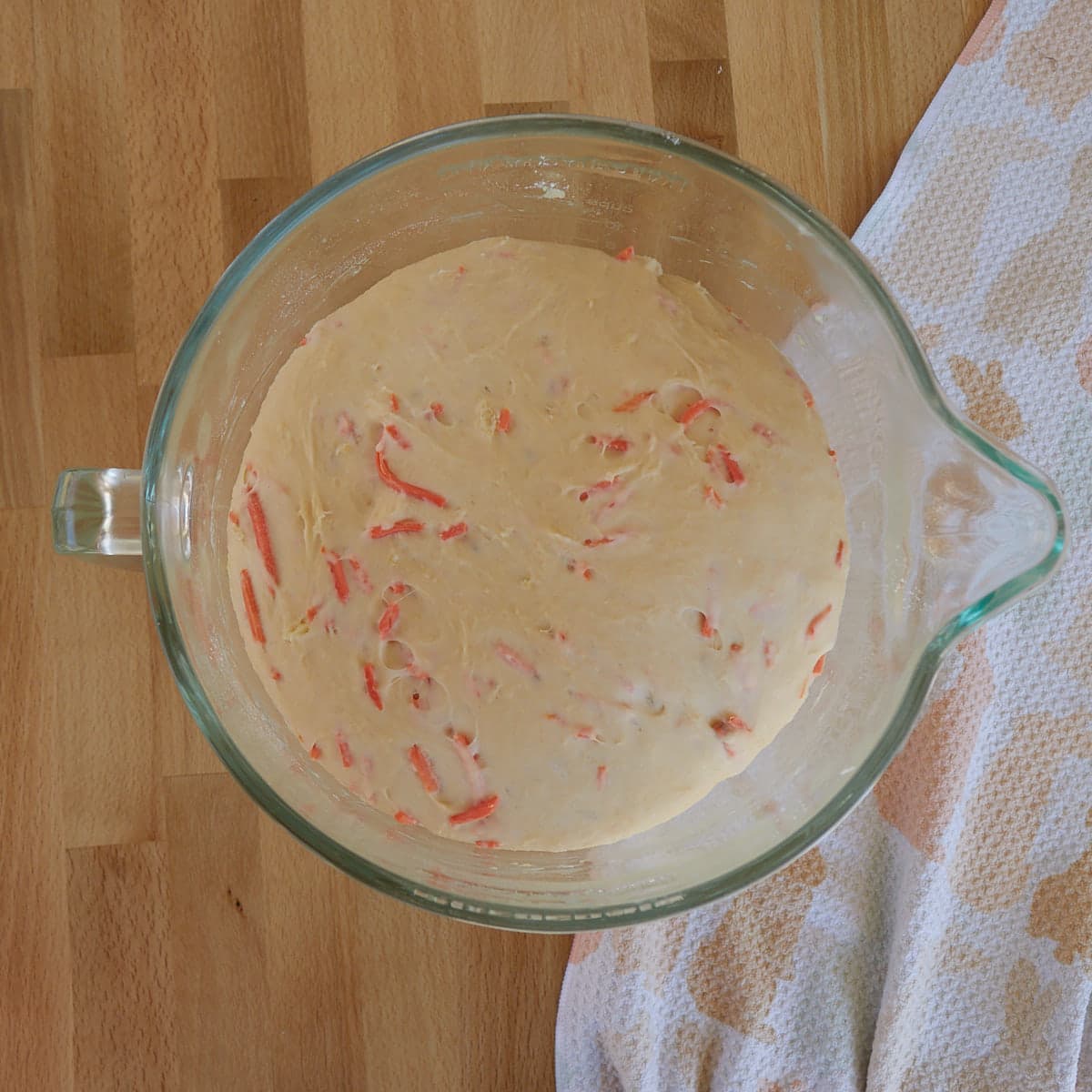 Carrot cake cinnamon roll dough in a glass bowl on a wood board after the first rise. 