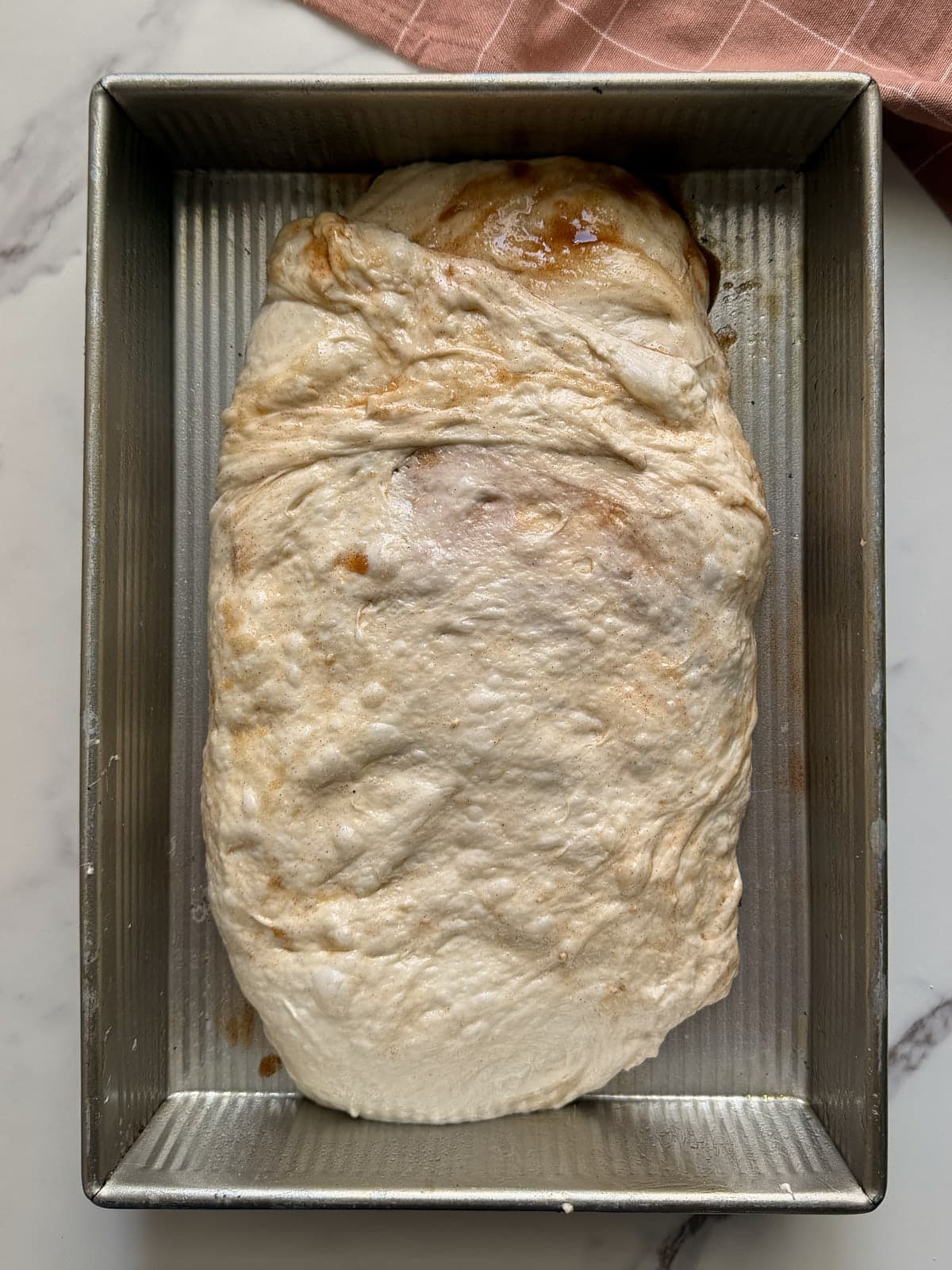 Sourdough cinnamon roll dough in a metal 9x13 pan before the second rise.