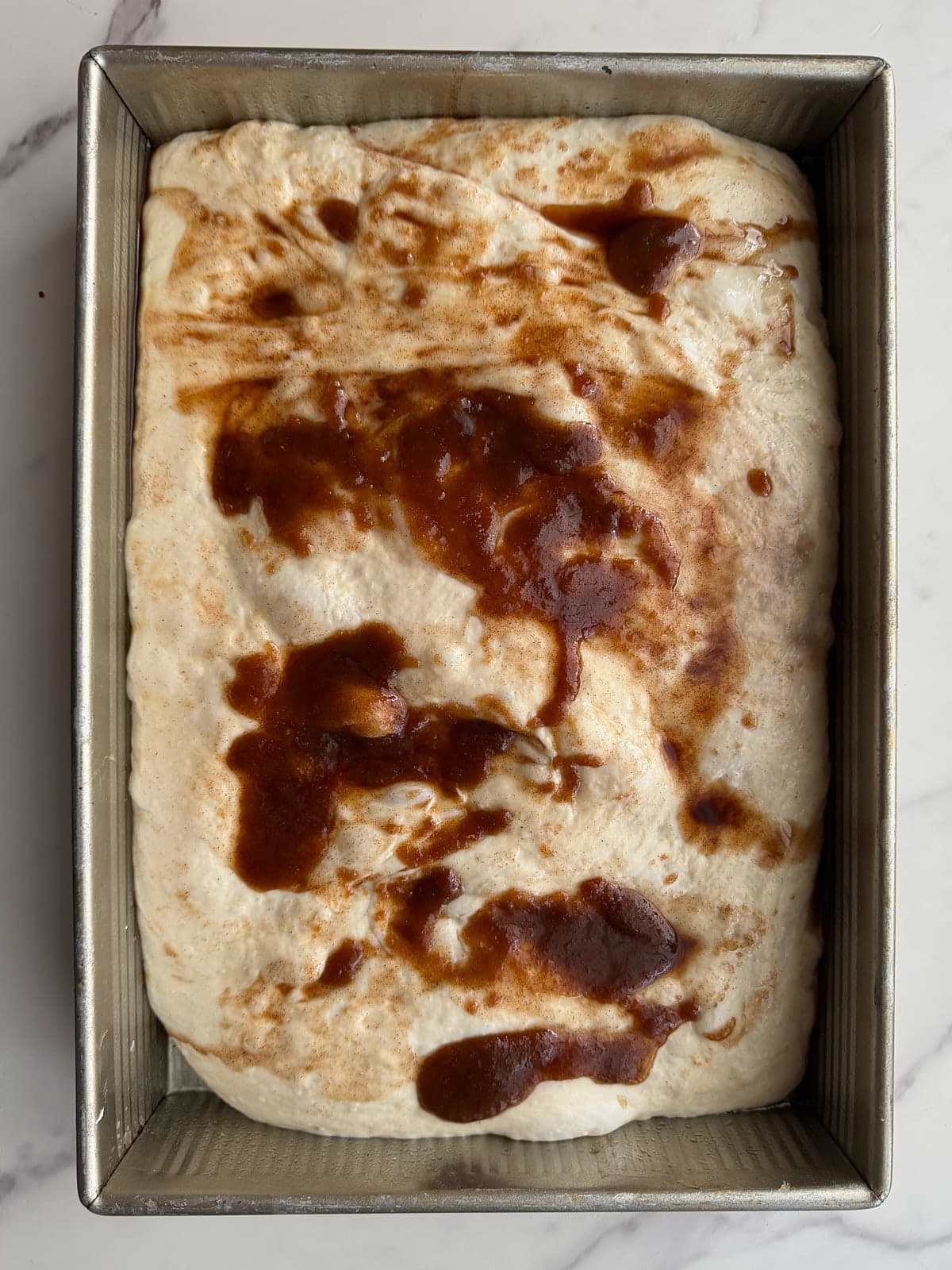 Sourdough cinnamon roll dough in a 9x13 pan with cinnamon sugar on top after the second rise.