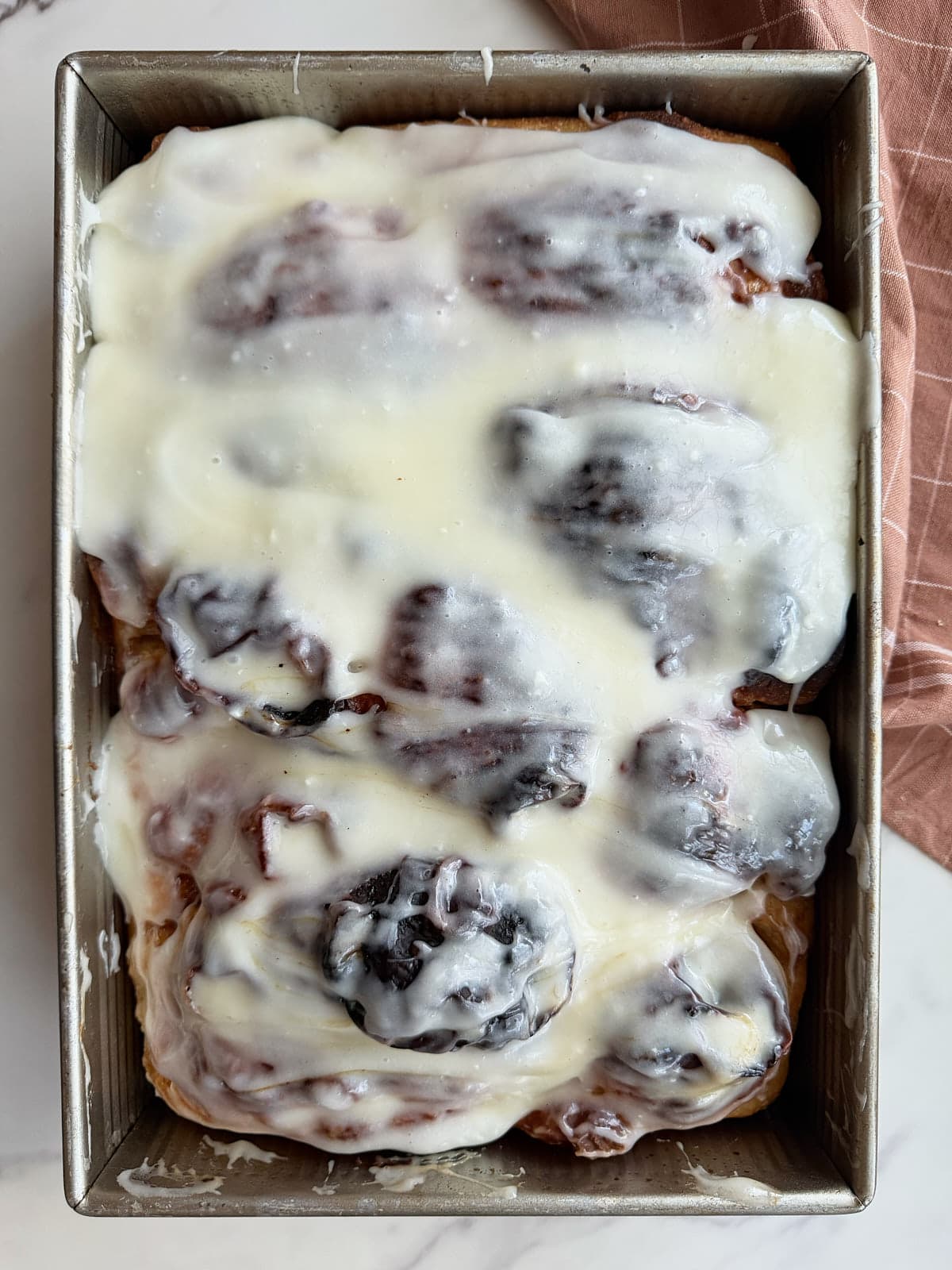 Cream cheese icing on cinnamon roll focaccia in a 9x13 pan.