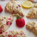 Strawberry lemon sourdough scones on a white surface with a fresh strawberry and a lemon slice.