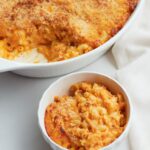 One white bowl filled with veggie sourdough mac and cheese next to a white casserole dish