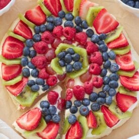 Sourdough Fruit Pizza with blueberries, kiwi, strawberries, raspberries and grapes on top of brown parchment paper.