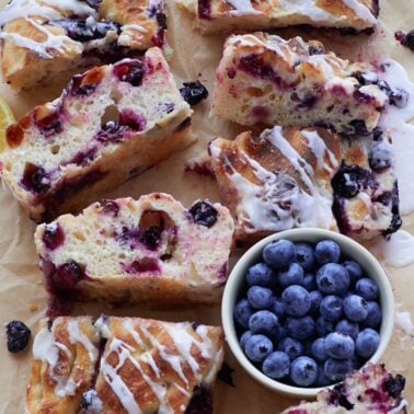 Lemon Blueberry Sourdough Focaccia slices on brown parchment paper next to a small bowl of blueberries.