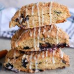 Three Blueberry Coffee Cake Sourdough Scones stacked on top of each other next to a blue and white linen towel.