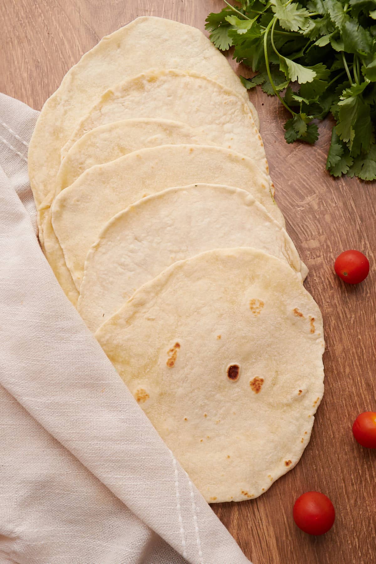 Sourdough tortillas lined in a row on wood with tomatoes and cilantro. 