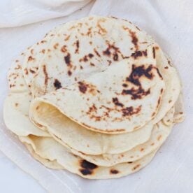 Sourdough Flour Tortillas stacked on top of each other on a linen napkin.