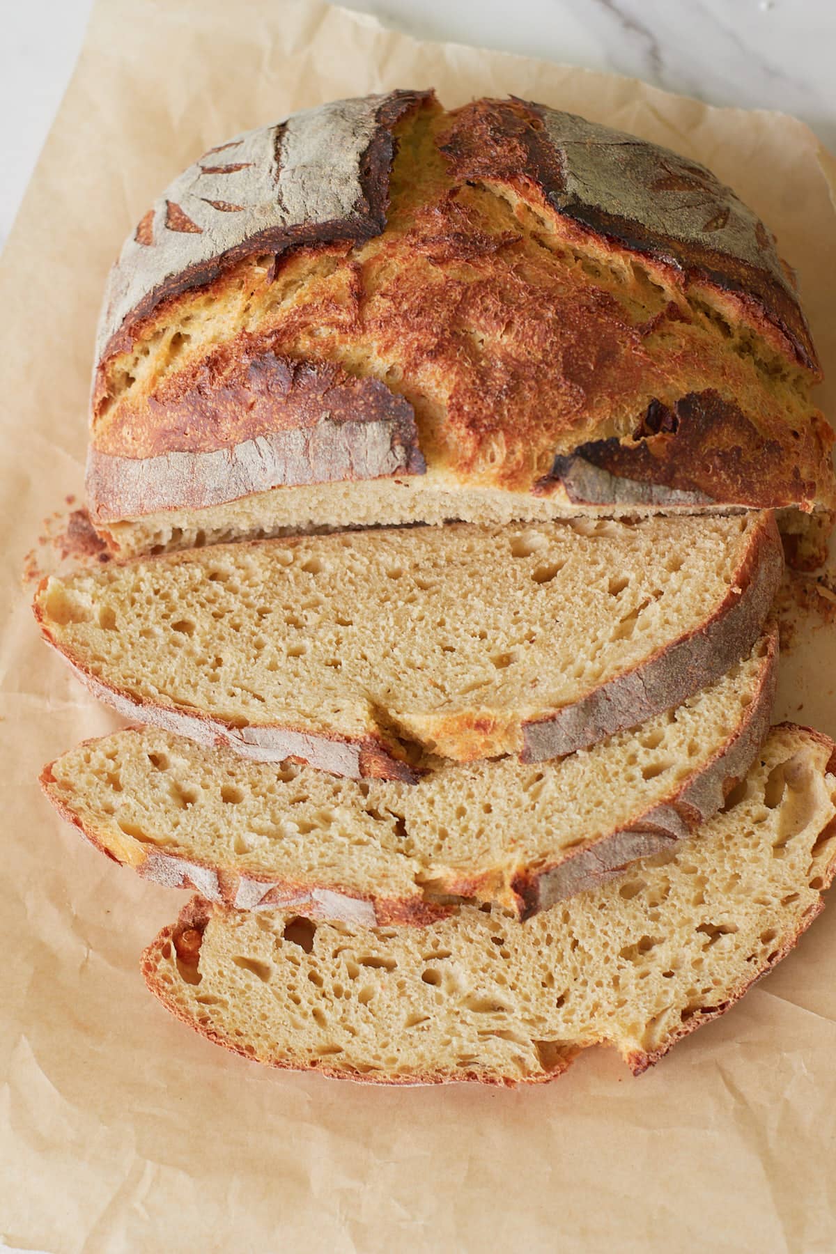 Loaf of Einkorn Sourdough Bread with three slices on top of brown parchment paper.