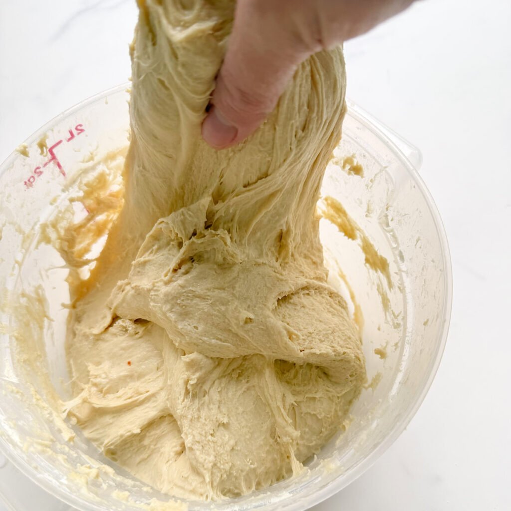 Hand pulling a portion of dough up for stretch and folds.
