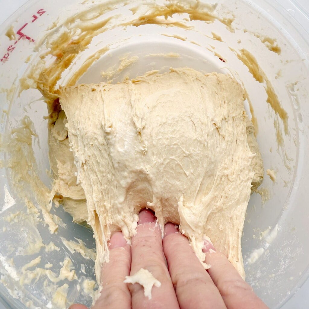 Hand pulling dough over top of itself during stretch and folds.