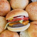 Cheeseburger made with Sourdough Hamburger Buns on top of a pile of freshly baked buns.