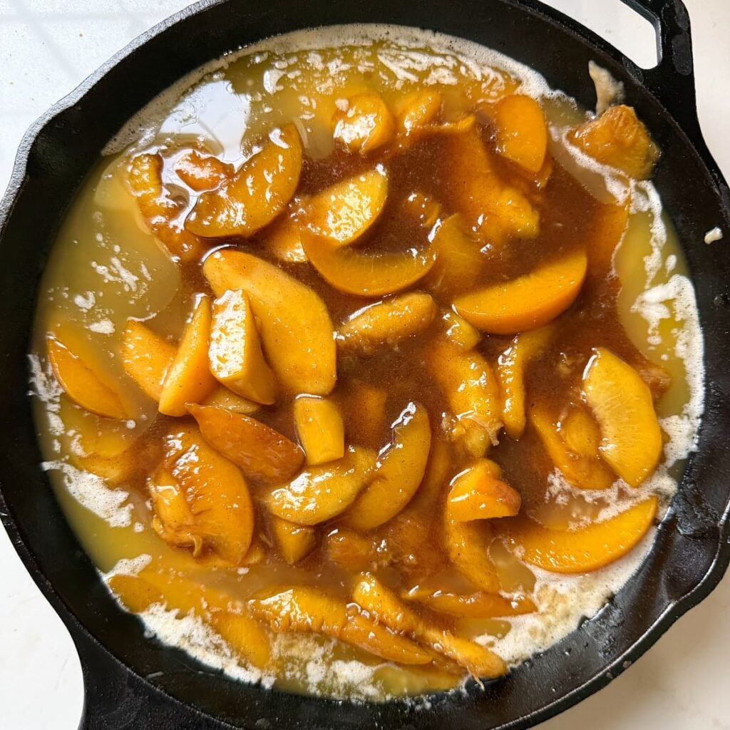 cooked peaches added on top of cobbler batter in a cast iron pan.