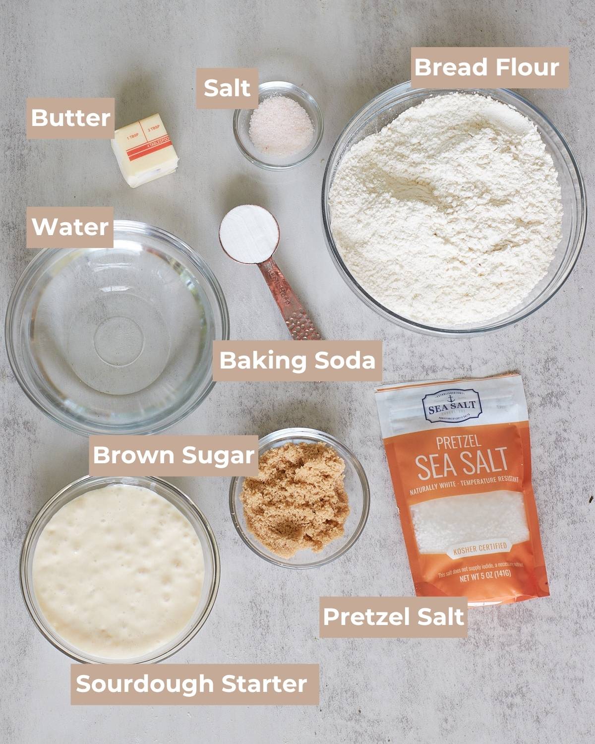Ingredients for Sourdough Pretzel Bites in clear bowls on a grey background.