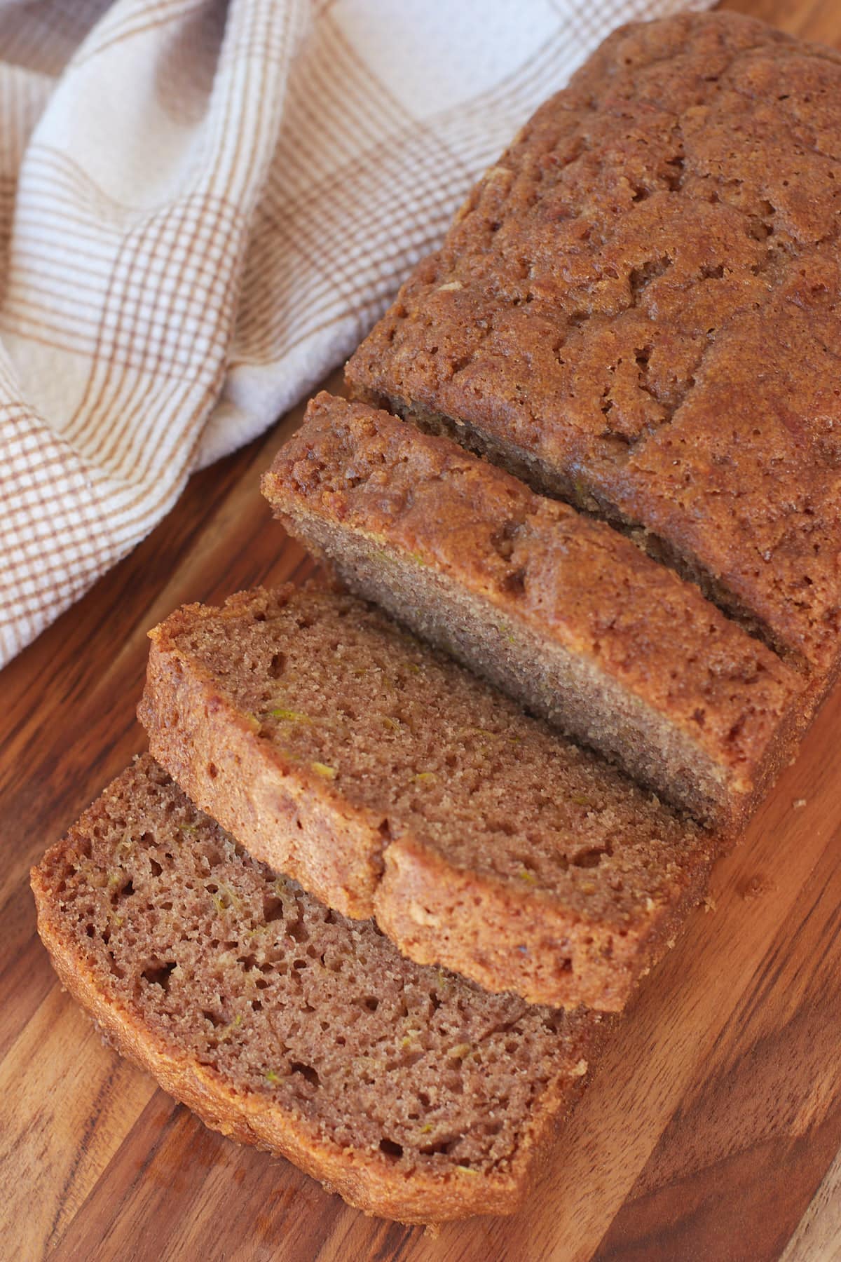 Sliced Sourdough Zucchini Bread on a wooden cutting board next to white and brown towel.