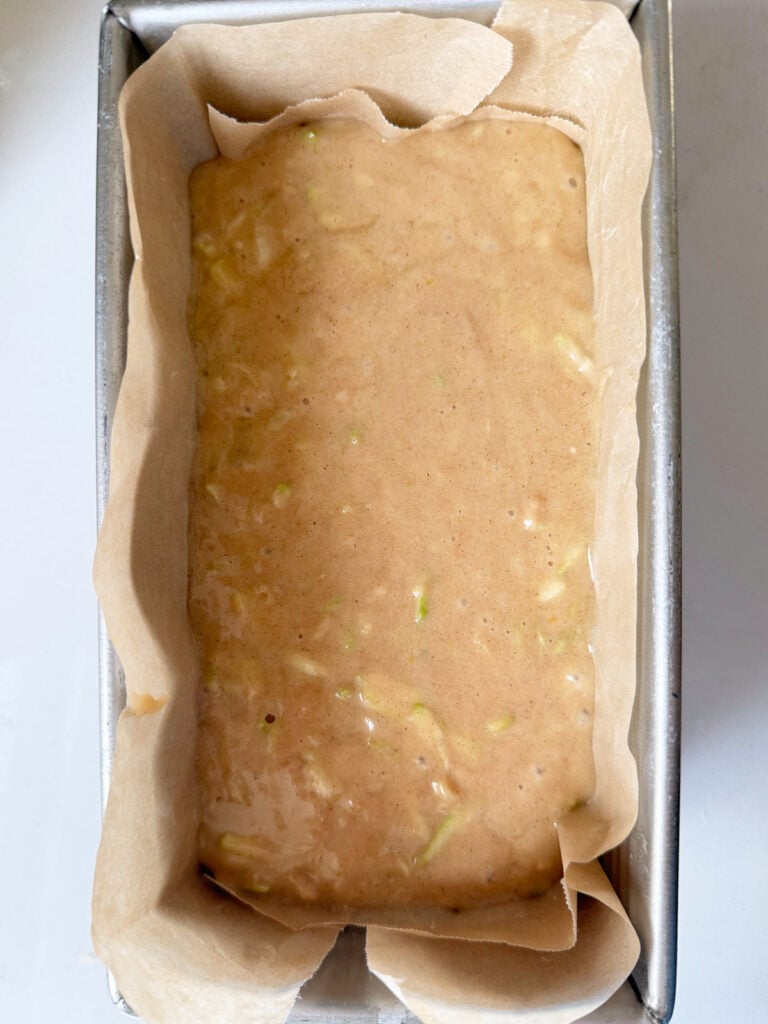 Batter for sourdough zucchini bread in a parchment-lined metal loaf pan.