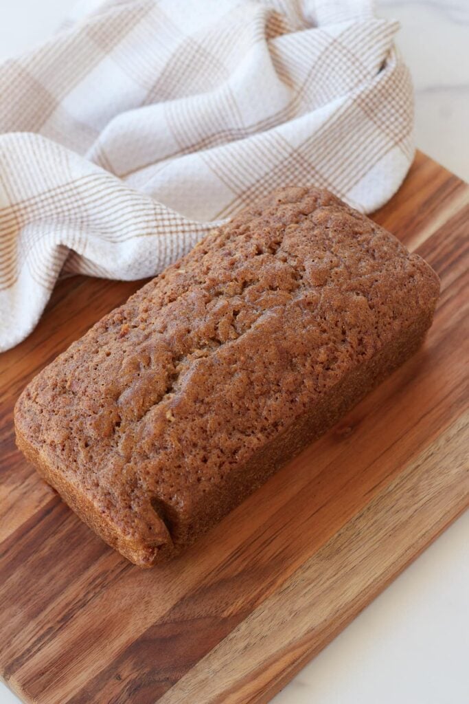 Freshly baked loaf of sourdough zucchini bread on wooden cutting board with a white and brown towel next to it.