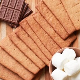 Sourdough Graham Crackers on a wooden board next to a small bowl of marshmallows and Hershey's chocolate.