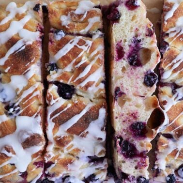 Slices of lemon blueberry sourdough focaccia with a drizzle of glaze on top of parchment paper.
