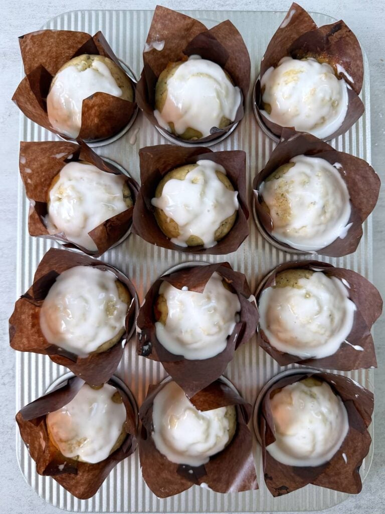 Lemon glaze added on top of Lemon Poppyseed Sourdough Muffins in metal muffin pan.