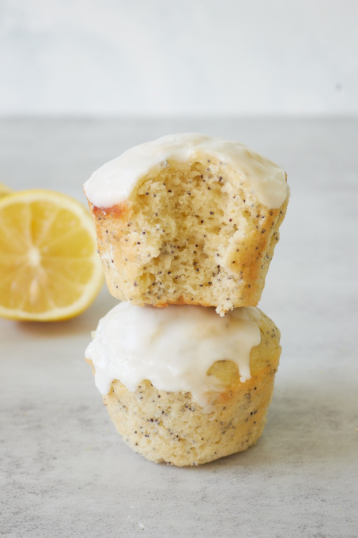 Two Lemon Poppyseed Sourdough Muffins stacked on top of each other with a bite taken out next to a slice of lemon.