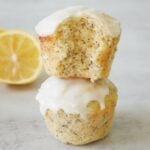 Two Lemon Poppyseed Sourdough Muffins stacked on top of each other with a bite taken out next to a slice of lemon.