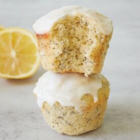 Two Lemon Poppyseed Sourdough Muffins stacked on top of each other with a bite taken out next to a slice of lemon.