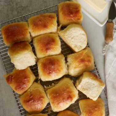 Same day sourdough dinner rolls on top of a wire rack next to a stick of butter and butter knife.