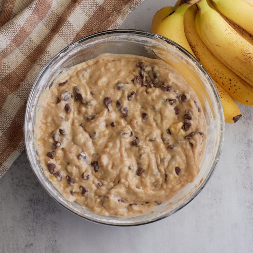 Sourdough Banana Muffin batter with chocolate chips added in a clear bowl.