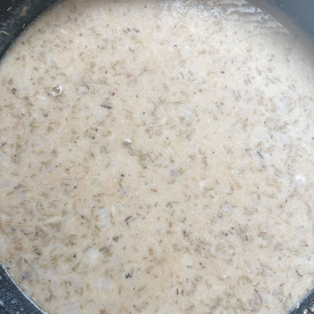 Chicken broth added to sauteed onions and seasoning in a cast iron skillet.