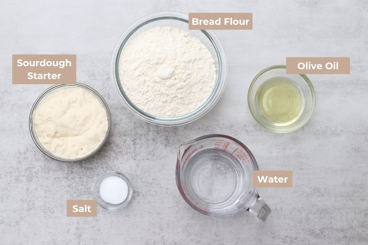 Ingredients for Sourdough Focaccia in clear bowls on a grey background.
