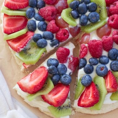 Sourdough fruit pizza with a slice cut out of it on top of brown parchment paper.