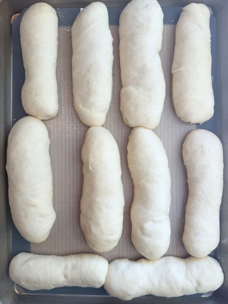 Sourdough hot dog buns on a sheet pan after the second rise.