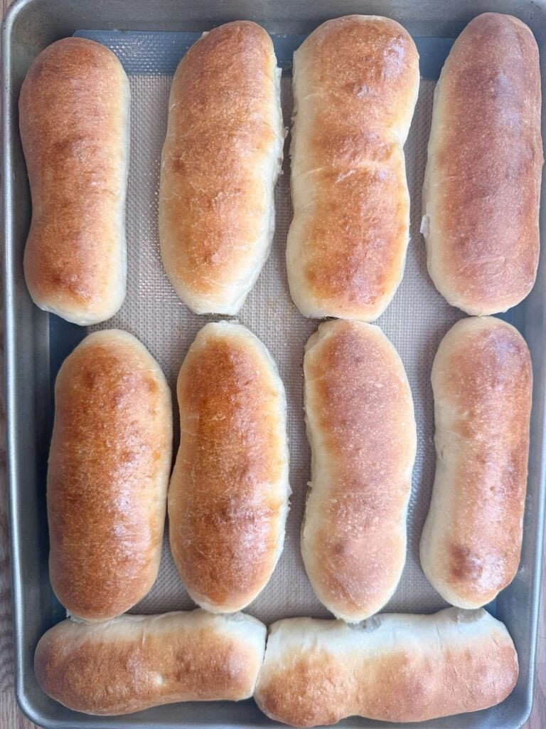 Freshly baked sourdough hot dog buns on a sheet pan.