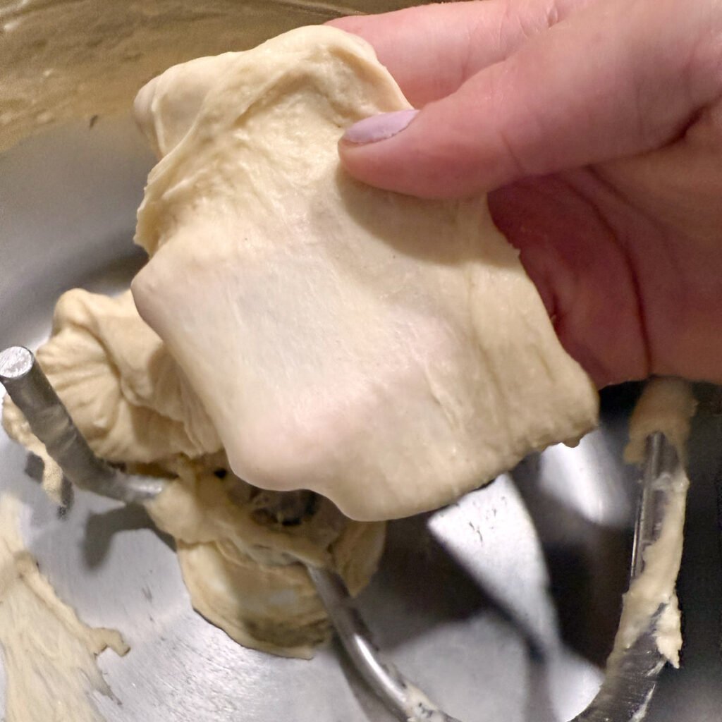 Hand holding dough doing the windowpane test.