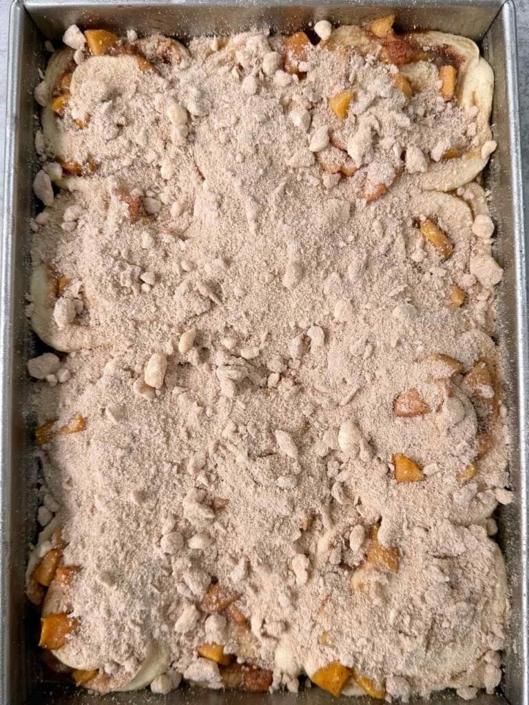 Crumb topping added on top of unbaked sourdough peach cobbler cinnamon rolls.