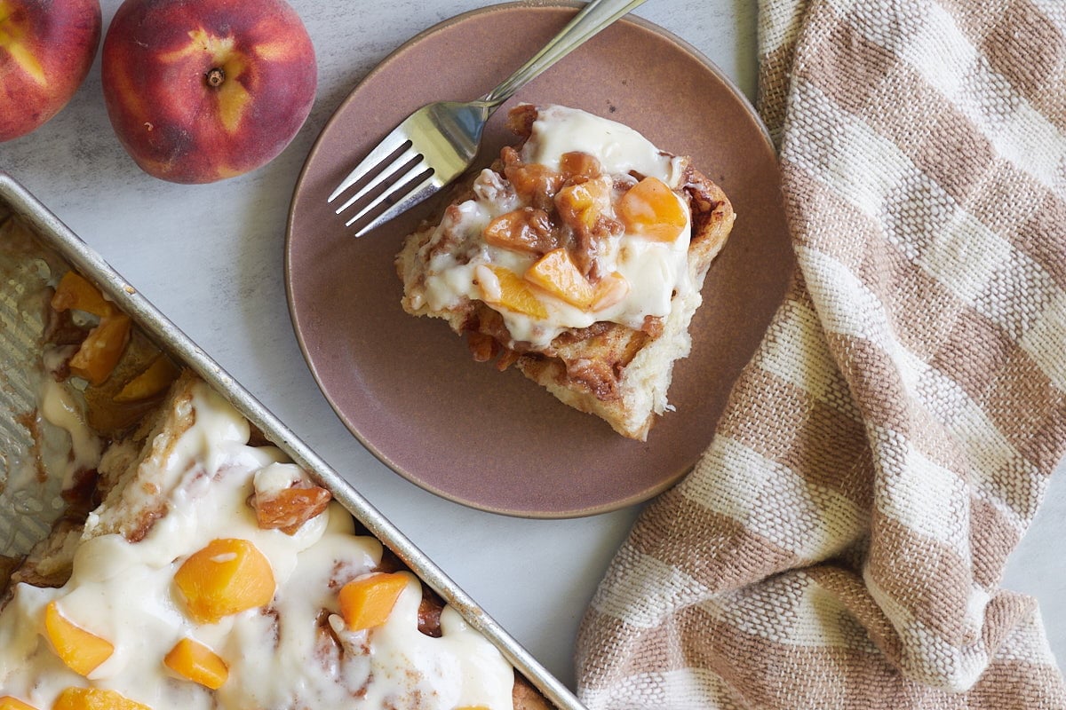 Sourdough peach cobbler cinnamon roll on a brown plate next to a 9x13 pan.