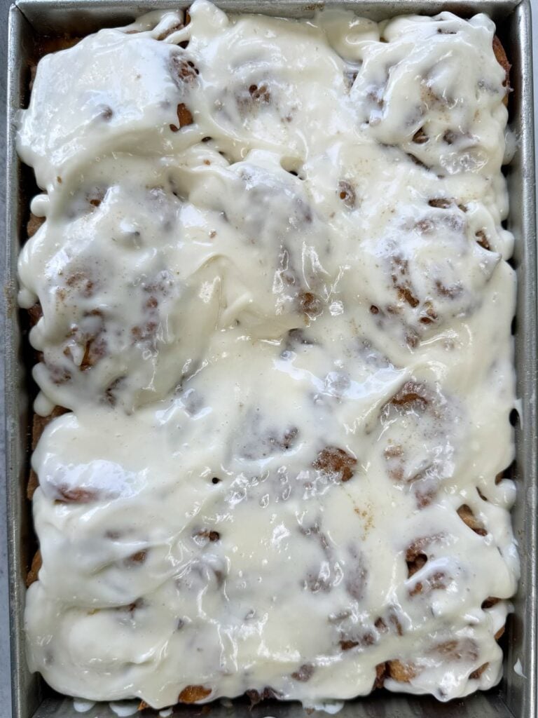 Cream cheese frosting on top of freshly baked sourdough peach cobbler cinnamon rolls.