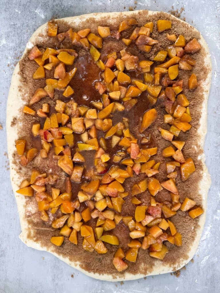 Cinnamon roll dough rolled into a rectangle with a layer of butter, cinnamon, sugar, and peach filling.