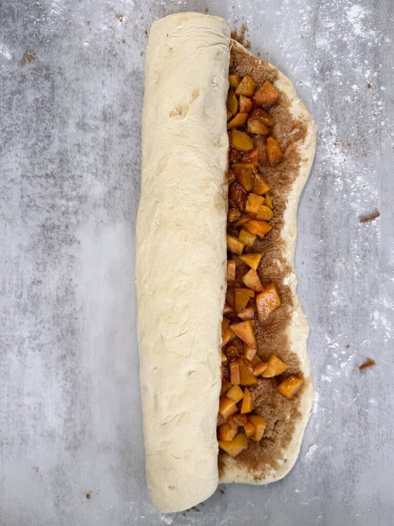Rolling sourdough cinnamon roll dough with peach filling.