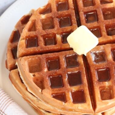 Two Sourdough protein waffles stacked on top of each other with butter on top on a white plate.