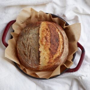 Freshly baked same day sourdough bread on parchment paper in a red bread oven.
