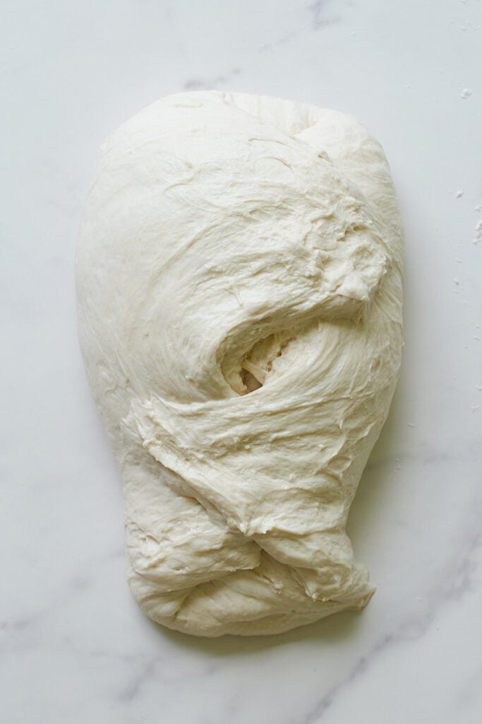 Shaping sourdough bread dough on a white surface.