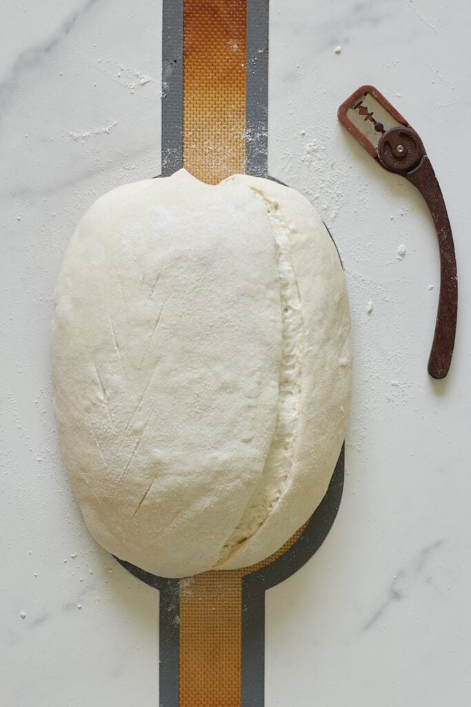Sourdough bread before baking on a bread sling with scores in the dough next to a bread lame.