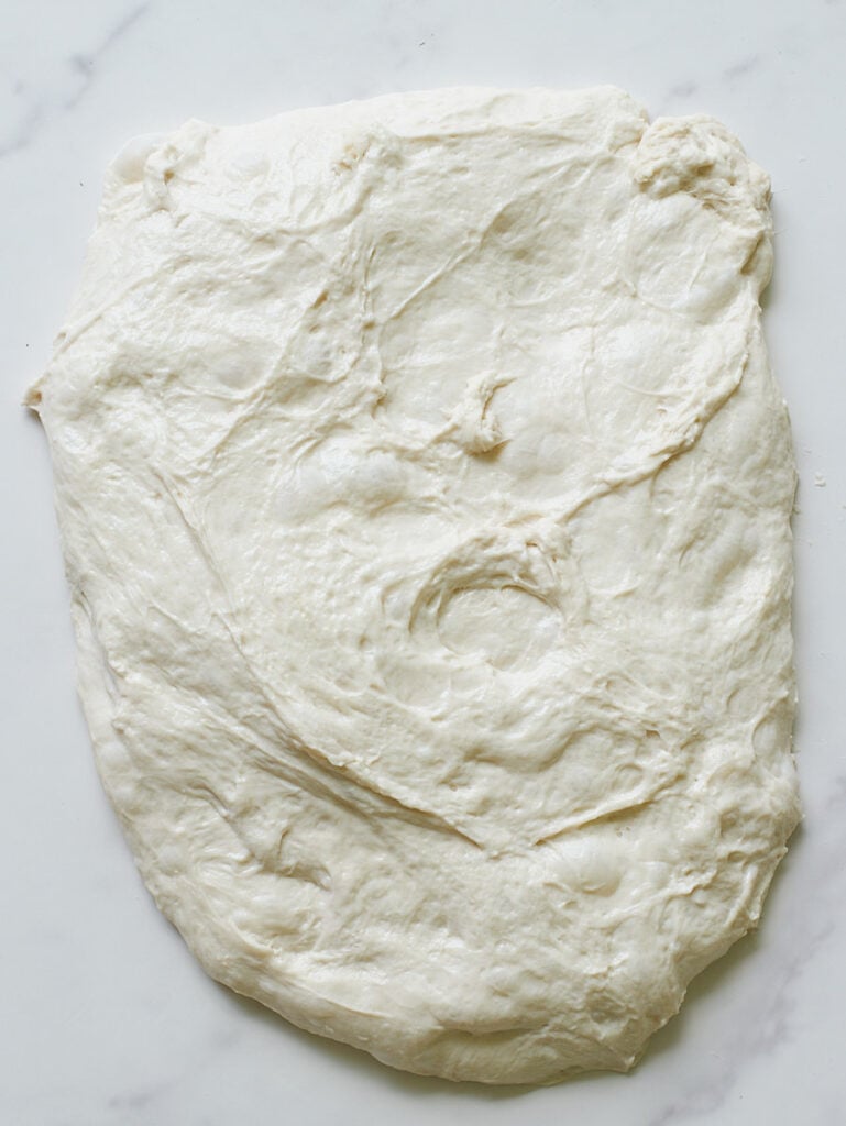 Sourdough bread dough spread into a chubby rectangle for shaping.