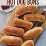 Sourdough Hot Dog Buns on a wooden board next to a plate of hot dogs.