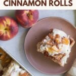 Sourdough peach cobbler cinnamon roll on a brown plate next to fresh peaches.